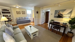 A living room with a sofa, coffee table, and a dining area with a table and chairs. There is a bookshelf and a star decoration on the wall. - Entire Historic 5 Bed/ 5 Bath Inn Sleeps 17 5 Bedroom Home (Newport)