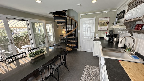 A modern kitchen with a dark countertop, white cabinets, and a built-in stove. There is a dining area with a table and chairs, and a staircase leading to an upper level. - Entire Historic 5 Bed/ 5 Bath Inn Sleeps 17 5 Bedroom Home (Newport)