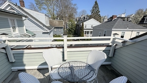 Een houten terras met een ronde tafel en vier rieten stoelen.