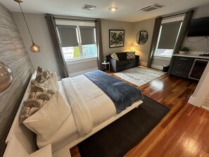 Quarto com cama, mesa de cabeceira, sofá, televisão e janela com cortinas.