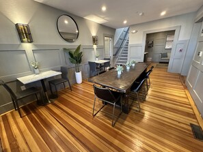 Uma área de refeições moderna com chão de madeira, uma mesa central com cadeiras e uma escada que leva a um andar superior.