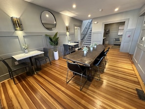 Un comedor moderno con suelo de madera, una mesa central con sillas y una escalera que sube a un nivel superior.