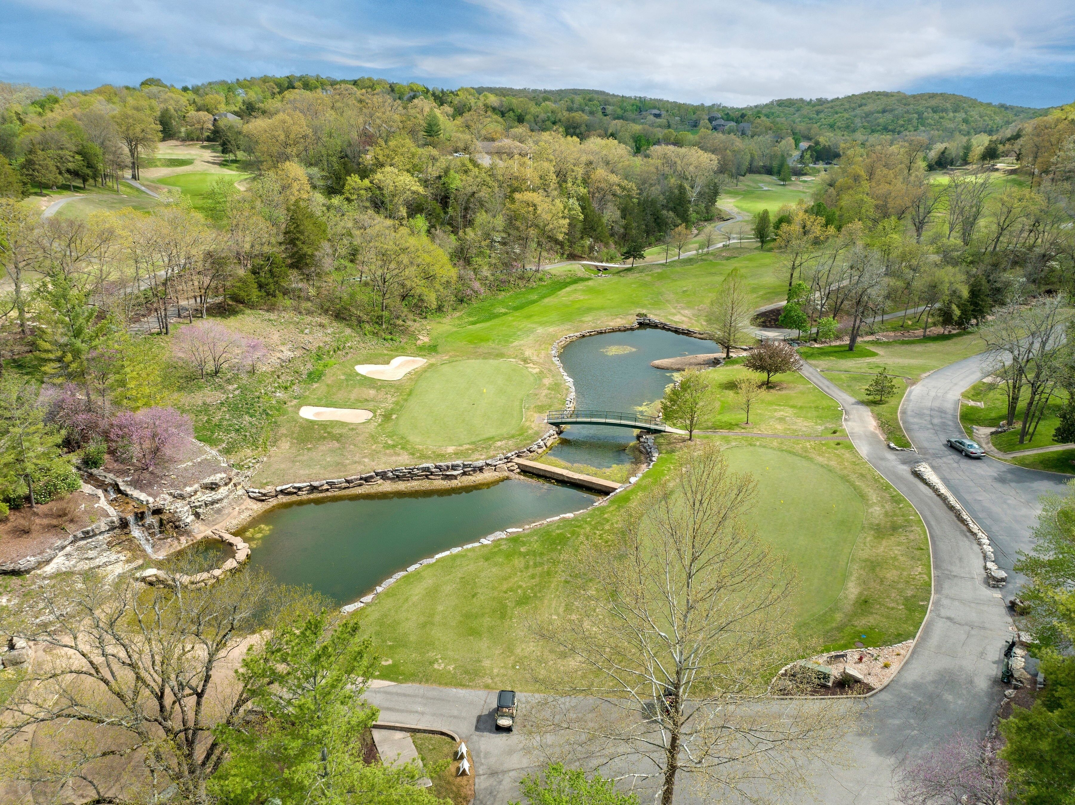 Un parcours de golf avec un étang, un pont et une route sinueuse.