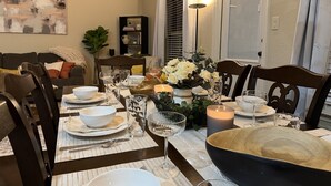 A dining table set with white plates, bowls, and glassware, surrounded by dark wooden chairs. - Pet-Friendly 3BR Fire Pit & Games Near Sea World (San Antonio)