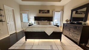 A bedroom with a dark wooden bed, a white rug, a dresser, and a ceiling fan. - Pet-Friendly 3BR Fire Pit & Games Near Sea World (San Antonio)