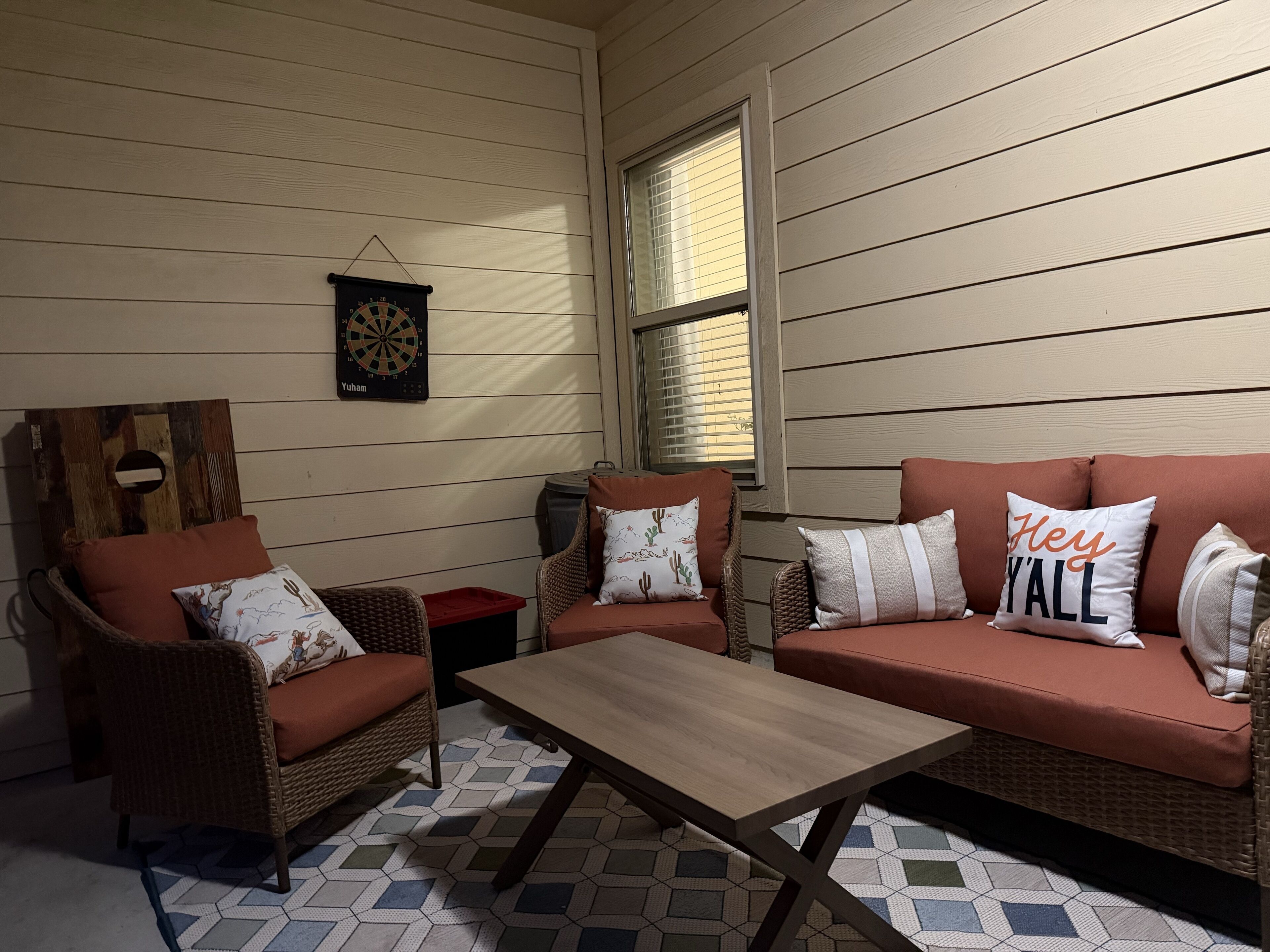 A cozy room with two wicker sofas, a wooden coffee table, and a dartboard on the wall.