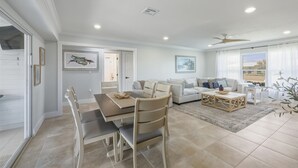 A spacious living area with a dining table, chairs, a sofa, and a coffee table. There is a ceiling fan, a window with curtains, and artwork on the walls. - Jun931 3 Bedroom Home (Punta Gorda)