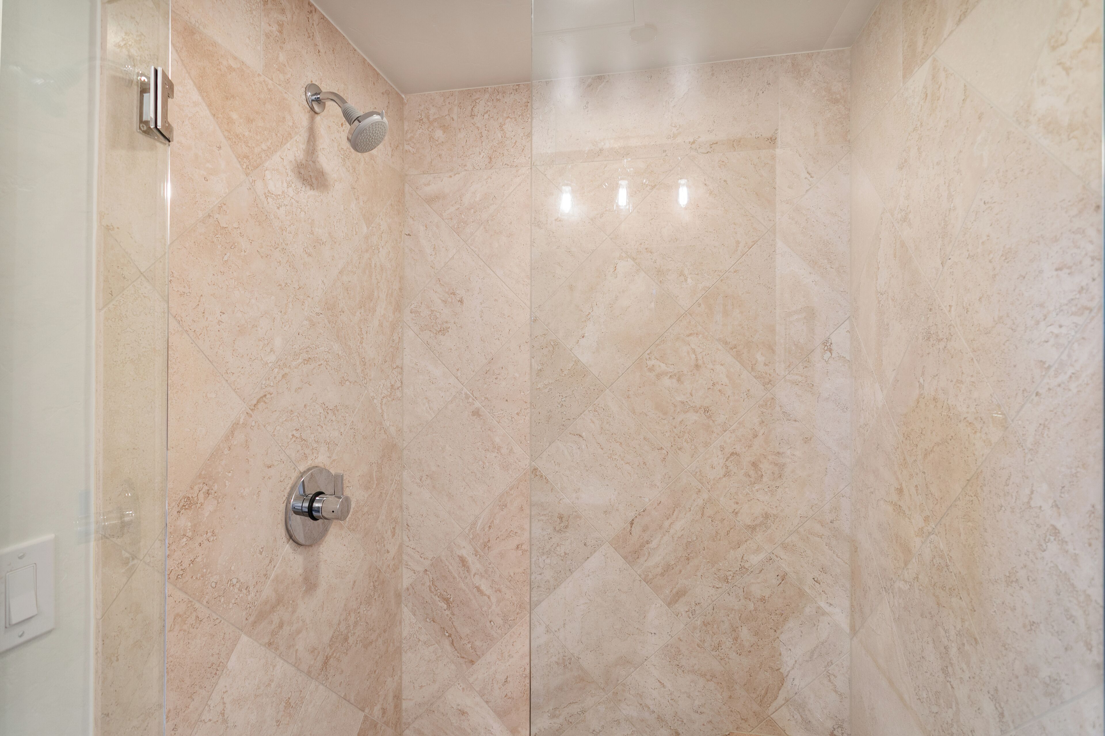 Ducha con azulejos color beige y cabezal de ducha cromado.