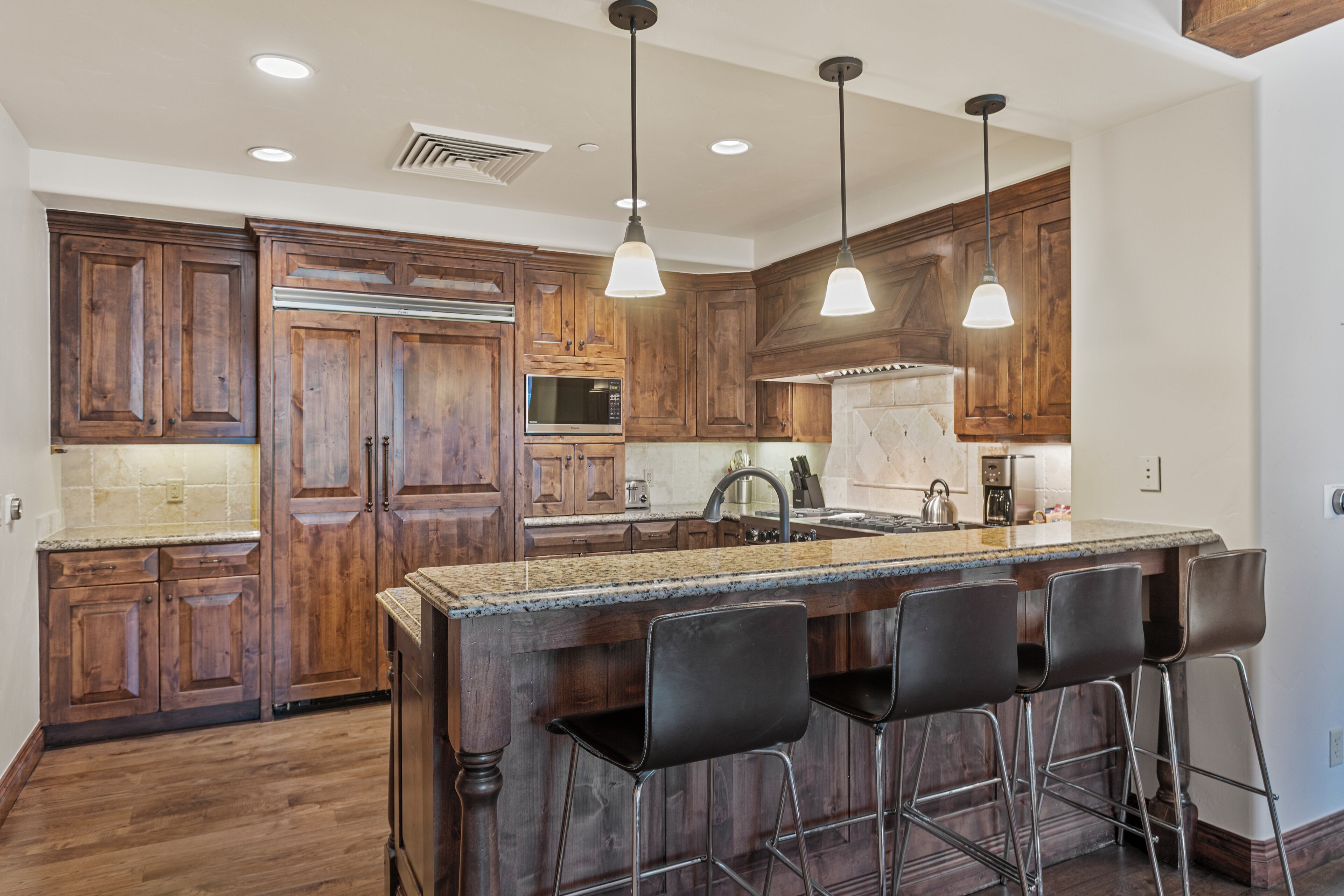 A kitchen with wooden cabinets, a granite countertop, and bar stools.