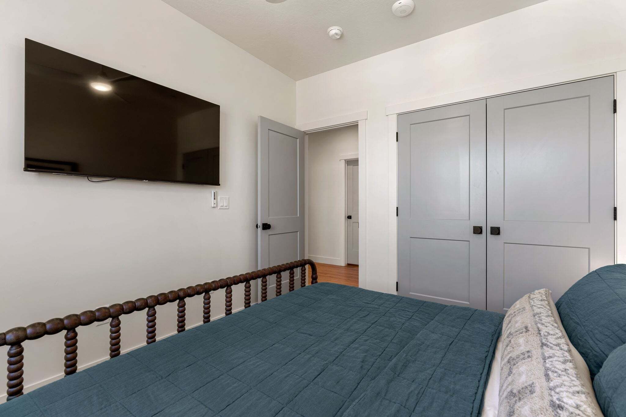 A bedroom with a bed, a TV mounted on the wall, and two doors.