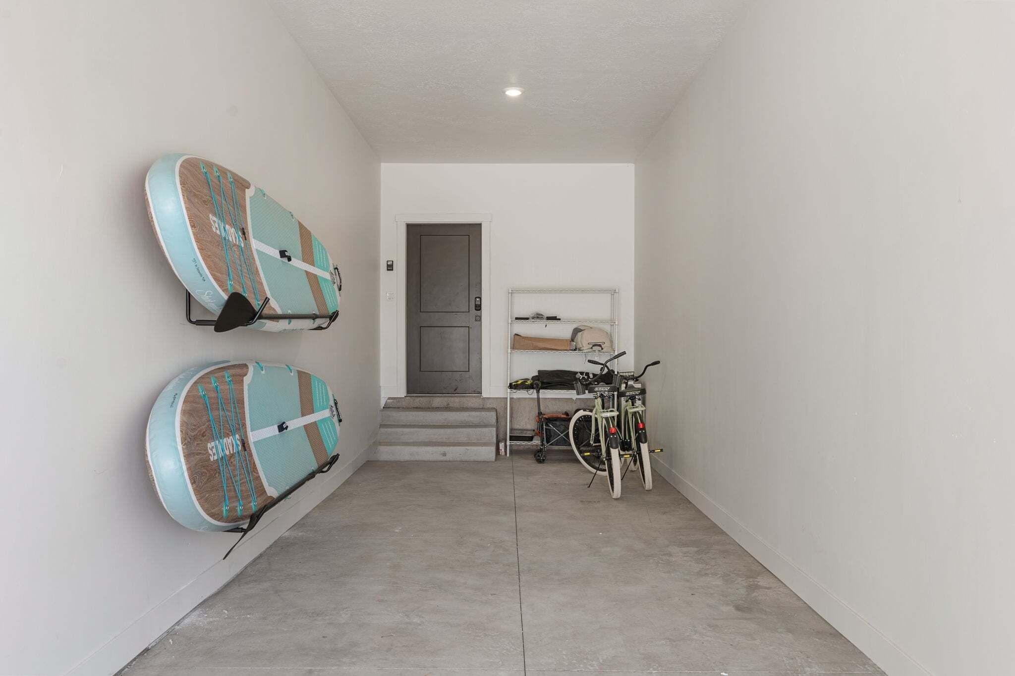 Un couloir dans lequel on peut voir deux planches de surf accrochées au mur, un vélo et une porte qui donne sur une autre pièce.