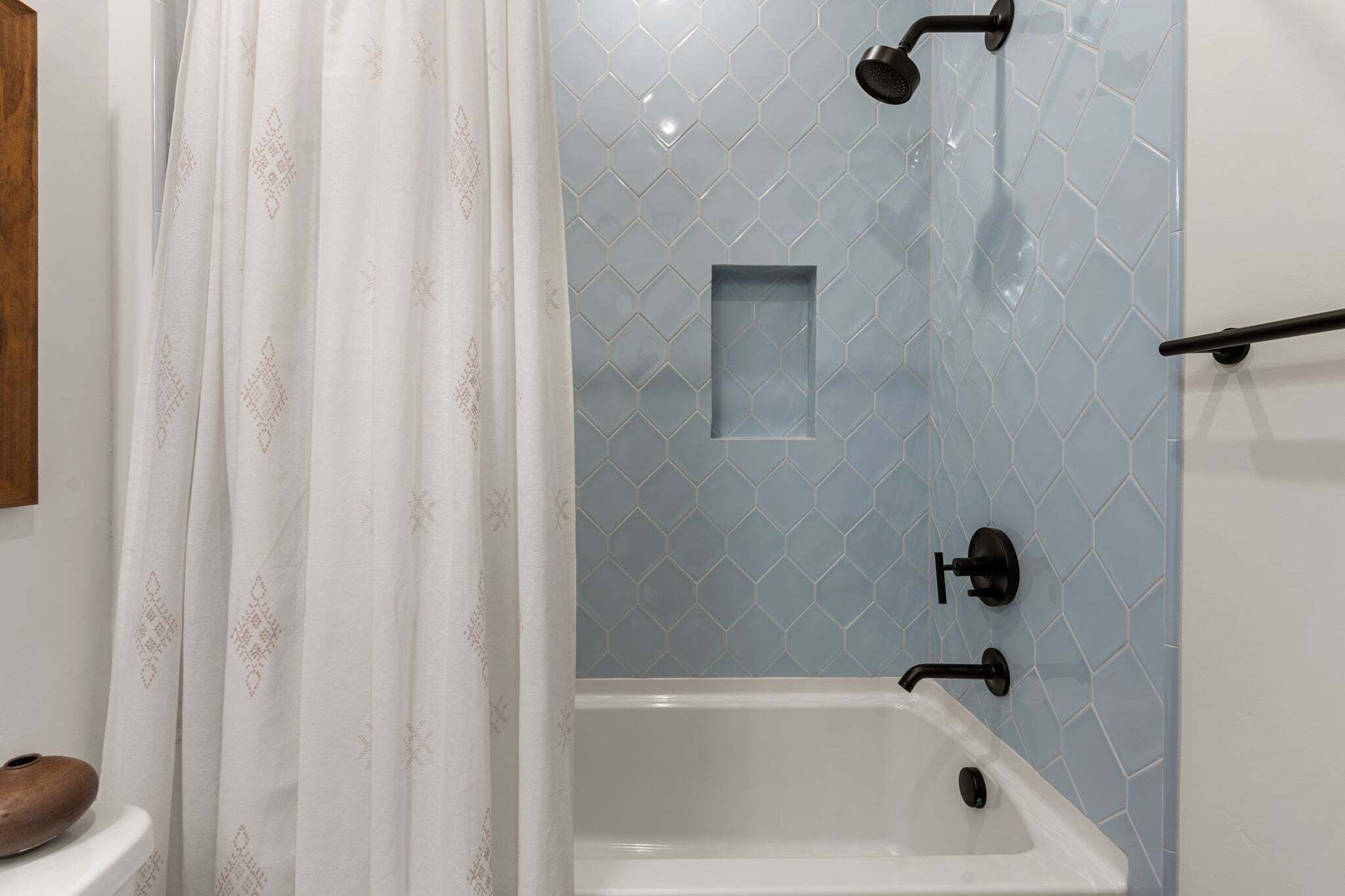Een badkamer met een witte badkuip, een douche met glazen wanden en een gordijn met een patroon.