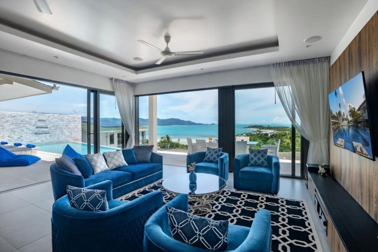 A modern living room with blue sofas, a round coffee table, and a large window offering a view of the sea and mountains.