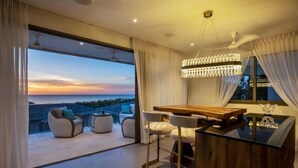 A modern dining area with a glass table, white chairs, and a view of the sunset over the ocean. - Sunset & Seaview Poseidon’s Penthouse (Chang Wat Surat Thani)