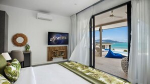 A hotel room with a large bed, a TV on the wall, a view of the beach, and a balcony with a blue chair. - Sunset & Seaview Poseidon’s Penthouse (Chang Wat Surat Thani)