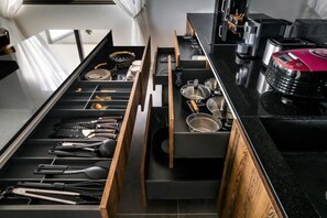A kitchen with a black countertop, wooden drawer, and various utensils. - Sunset & Seaview Poseidon’s Penthouse (Chang Wat Surat Thani)