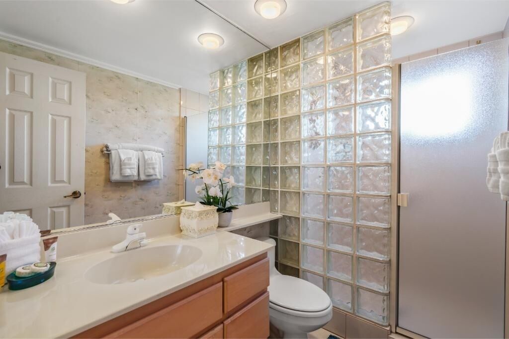 A bathroom with a white sink, a mirror, a toilet, and a glass shower enclosure.