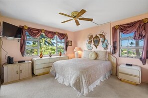 A bedroom with a bed, a ceiling fan, a television, and a window with curtains. - Menehune Shores, #301 2 Bedroom Condo (Kihei)