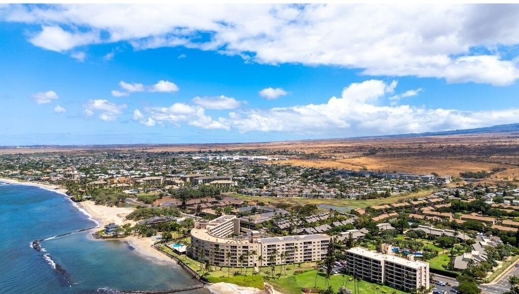 An aerial view of a coastal resort area with multiple buildings, including a large hotel with a circular central building and several smaller structures.