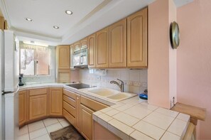 A kitchen with wooden cabinets, a double sink, and a window with a view. - Menehune Shores, #301 2 Bedroom Condo (Kihei)