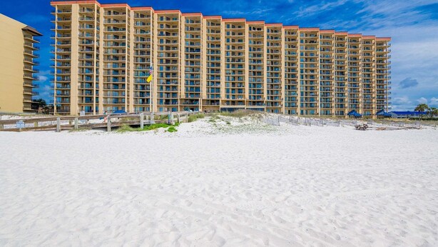 Ein Hochhaus-Hotel mit mehreren Balkonen direkt an einem Sandstrand.