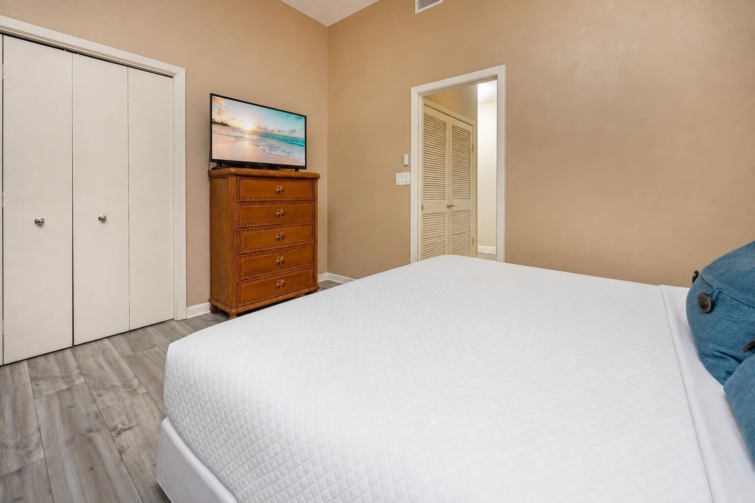 A bedroom with a bed, a dresser, a television on the wall, and a closet.