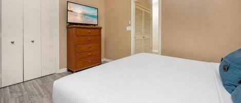 A bedroom with a bed, a dresser, a television on the wall, and a closet.