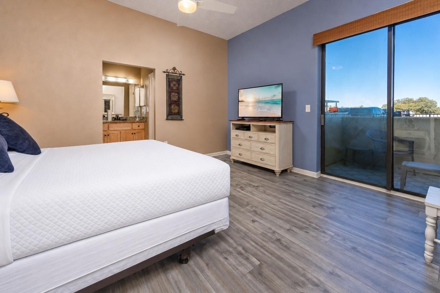 A bedroom with a bed, dresser, TV, and a balcony with a view.