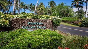 Señal de Waikoloa Colony Villas, con un muro de piedra, exuberante follaje y palmeras.