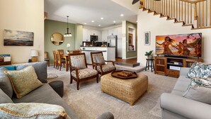 Una sala de estar con sofá, sillones, una mesa de centro, televisión y una escalera.