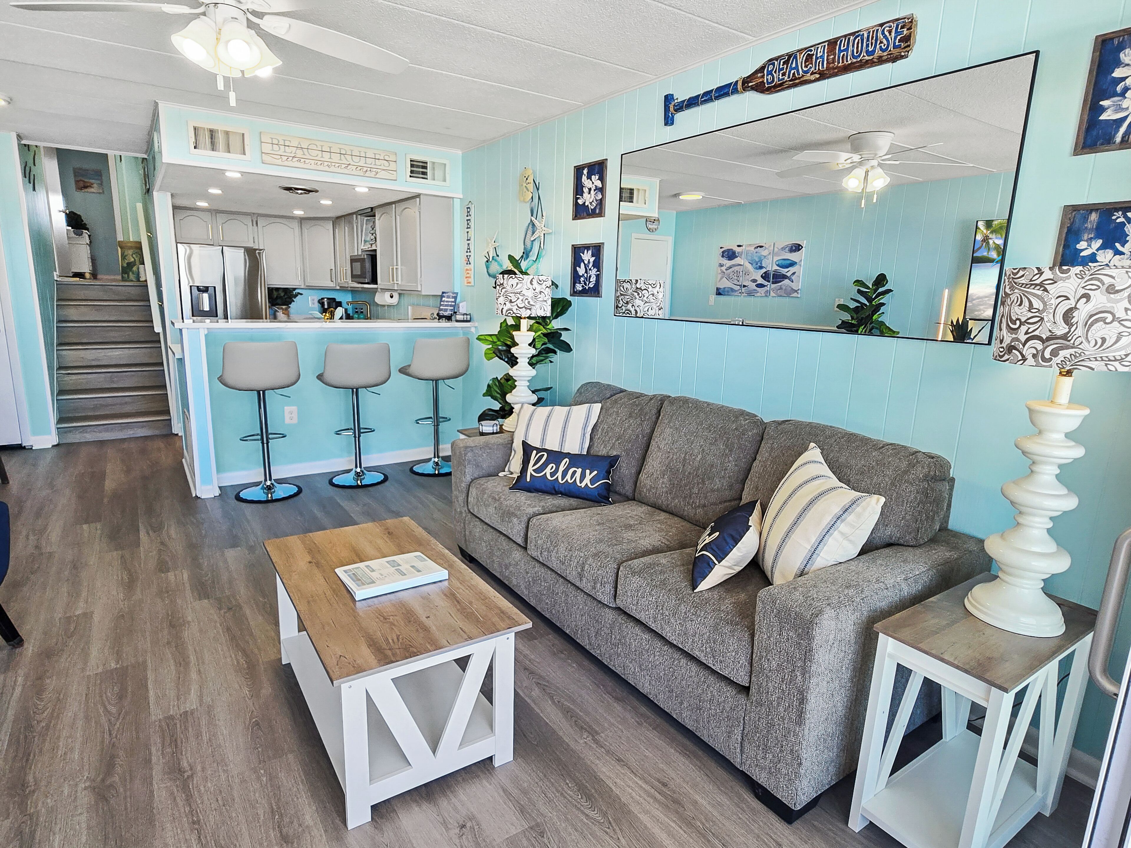 A living room with a grey sofa, a wooden coffee table, and a kitchen area with a bar stool set.