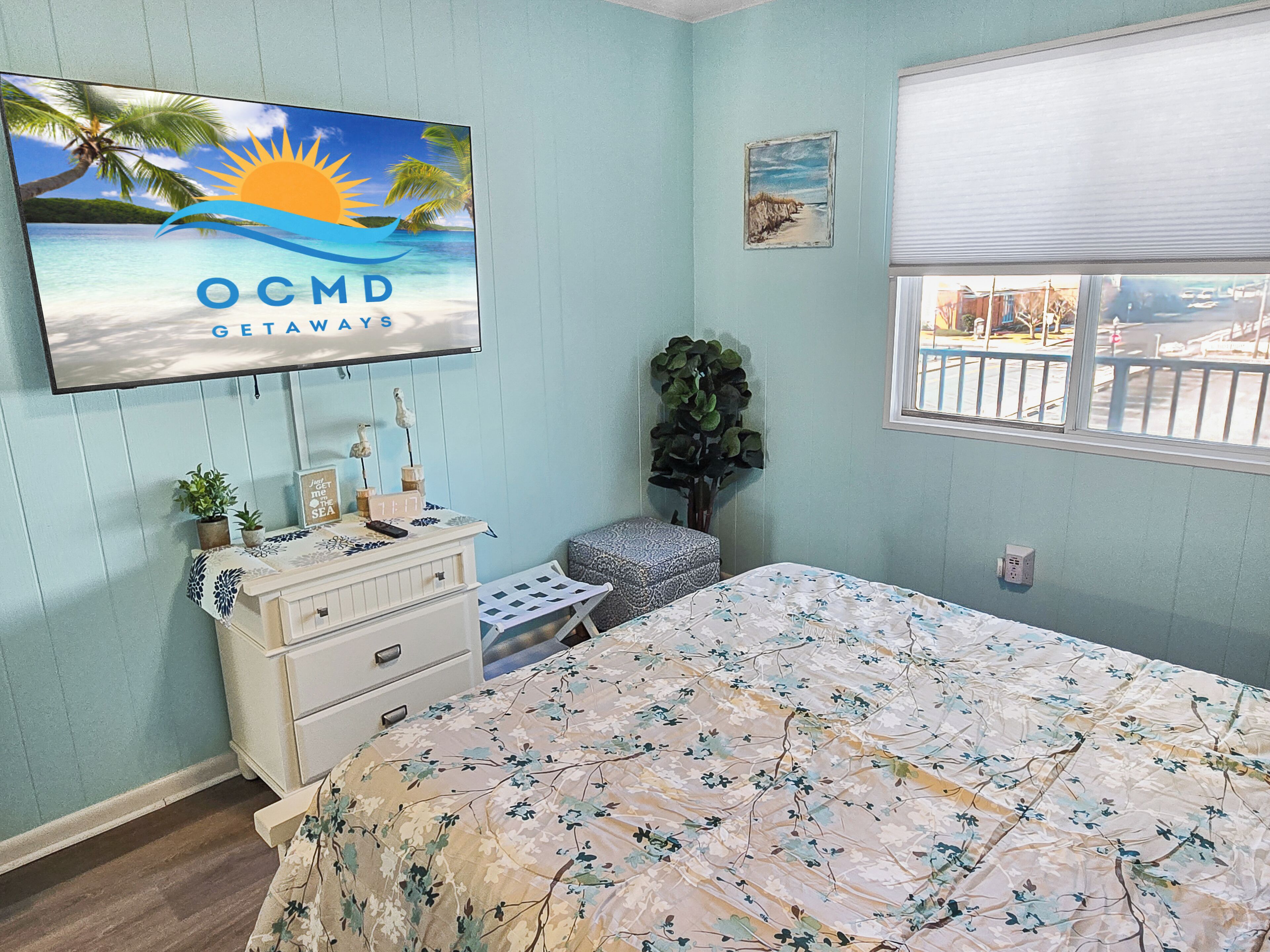 Un dormitorio con cama, cómoda y televisor mostrando 'OCMD GETAWAYS'.