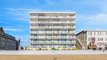 A multi-story hotel with balconies, a sandy ground in front, and a clear blue sky.