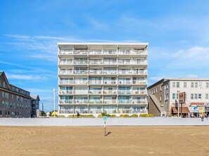 A multi-story hotel with balconies, a sandy ground in front, and a clear blue sky. - Oceanfront Second Floor Condo on the Boardwalk with Pool. Steps from the Ocean! El Capitan 204 (Ocean City)