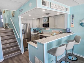A kitchen with a central island, stainless steel appliances, and a bar area with stools. - Oceanfront Second Floor Condo on the Boardwalk with Pool. Steps from the Ocean! El Capitan 204 (Ocean City)