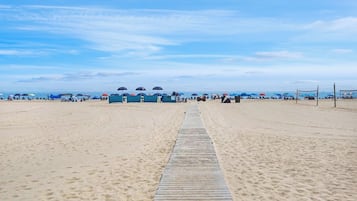 A beach with a wooden walkway leading to the water, umbrellas, and beach chairs.