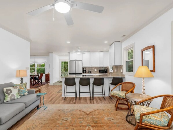 A modern kitchen with white cabinets, a central island with bar stools, and a dining area with a table and chairs. - Skipjack House | an ESVR property (Mcdaniel)
