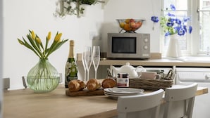 A kitchen counter with a vase of yellow tulips, a bottle of champagne, two glasses, a basket of croissants, a teapot, and a jar of jam. - Appledore Cottage  - Comfy and cosy dog friendly holiday home in the Cotswolds (Andoversford)