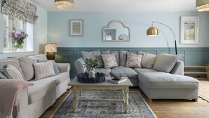 A living room with a light blue wall, a large mirror, and a round table with a basket and book. - Appledore Cottage  - Comfy and cosy dog friendly holiday home in the Cotswolds (Andoversford)