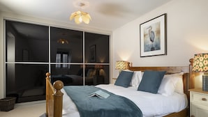 A bedroom with a large bed, a wooden headboard, a bedside table with a lamp, and a framed picture on the wall. - Appledore Cottage  - Comfy and cosy dog friendly holiday home in the Cotswolds (Andoversford)