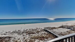 A beach with a clear sky, a sandy shore, and a wooden boardwalk leading to the water. - Ocean Breeze West #504 | Gulf-Front Balcony + Resort Amenities (Perdido Key)