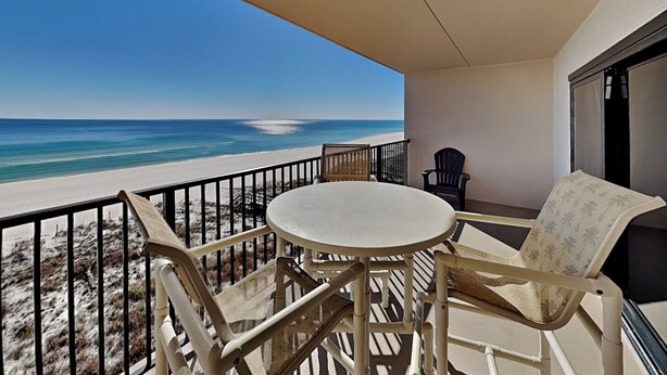 A balcony with a table and chairs, overlooking a beach with a clear view of the ocean. - Ocean Breeze West #504 | Gulf-Front Balcony + Resort Amenities (Perdido Key)
