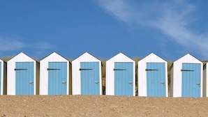 Fila de sis cabanes de platja amb portes blaves, parets blanques i terra de sorra al davant.