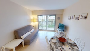 Un saló modern amb un sofà gris, una taula de dinar a punt per a quatre persones i un televisor sobre un moble.