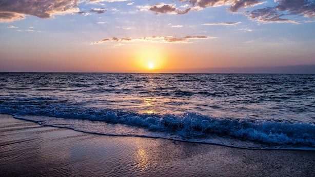 Un sol ponent-se sobre l'oceà amb onades que trenquen a la riba.