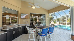 Cucina esterna con zona pranzo, comprensiva di tavolo e sedie, ventilatore a soffitto e vista su una piscina.