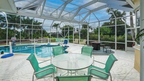 A covered outdoor area with a pool, green chairs, a table, and a fire pit. - 1338 Jamacia Road -  situated on the exclusive Island Country Club golf course. (Marco Island)