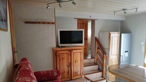 Una sala de estar con un sofá, un televisor sobre un mueble de madera, una escalera y un refrigerador.
