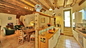 Een gezellige woonkamer met een houten plafond, een zithoek met een houten tafel en stoelen, en een keuken met witte kastjes en een betegelde vloer.
