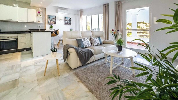 Un appartamento moderno con cucina, zona soggiorno con divano e tavolino, e un balcone con piante.